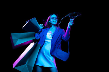 Young fashionable stylish happy woman with shopping bags isolated over dark background in neon...