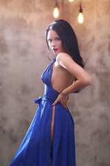 A girl with brown hair in a blue dress takes a photo shoot at home, posing in different poses