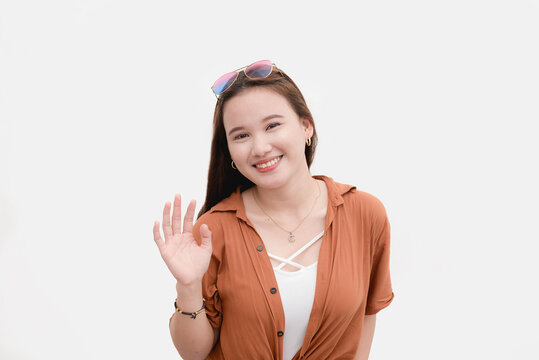 A Modern Congenial Young Asian Woman Saying Hi. Waving Her Hand. Isolated On White Backdrop.