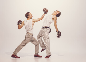 Portrait of two men playing, boxing in gloves isolated over grey studio background. Straight punch