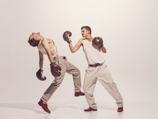 Portrait of two men playing, boxing in gloves isolated over grey studio background. Artistic...