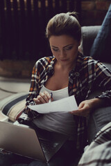 A brown-haired girl looks confident and professional while posing for photos on her sofa at home, checking important documents.