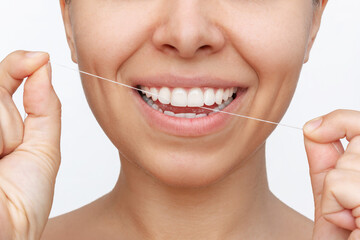Cropped shot of a young pretty caucasian woman flossing her teeth after meal with dental floss isolated on a white background. Dental health care, oral hygiene, evening routine. Dentistry concept