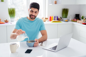 Portrait of peaceful satisfied man pouring fresh milk flakes plate enjoy free time morning house...