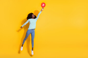 Full length portrait of carefree excited girl hand hold air balloon jump fly isolated on yellow color background