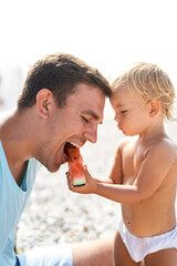 Little daughter feeding dad with watermelon on the beach