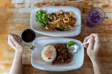 Hand holding a spoon The fork is placed on the dining table. Rice with fried pork, fried egg