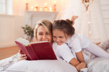 a mother and daughter reading a book on a bed, stock image, in the bedroom at a sleepover, full...