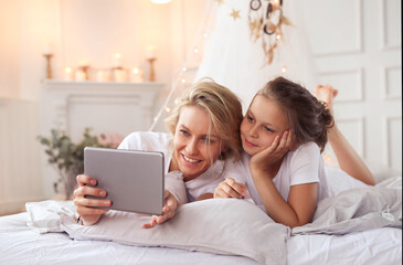 Fototapeta premium a woman and a little girl laying on a bed, having fun, film, elegant shot, photo of a beautiful, unique design, using a magical tablet