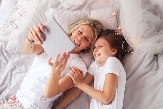 a woman and a little girl laying on a bed, having fun, film, elegant shot, photo of a beautiful, unique design, using a magical tablet