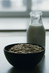 Raw oatmeal flakes in bowl with glass of milk