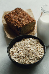 Whole grain bread with oatmeal flakes in bowl and glass of milk on the table