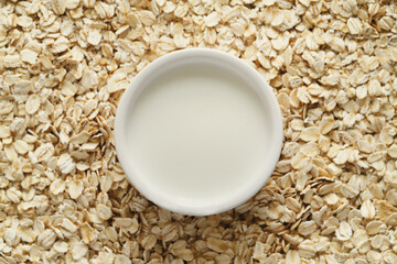 View from above on delicious milk in white bowl on oatmeal flakes background