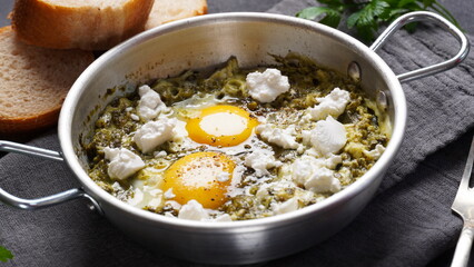 Green shakshuka with spinach, and feta in a frying pan on a table with bread