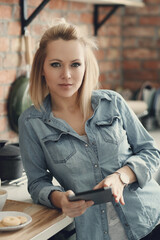 Image of a beautiful woman standing with digital tablet and looking at camera in the kitchen at home