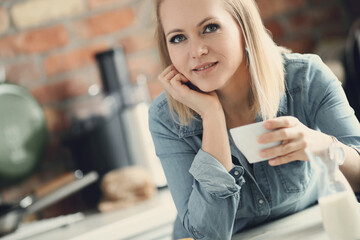 Picture of young blond woman with short hair looking at camera and holding a cup of tea in the...
