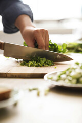 Women’s hands cut the greens on the board for the salad in the kitchen 