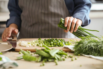 Women’s hands cut fresh green onion salad on the kitchen table