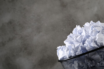 Many creased white paper balls in a trash can on a dark background