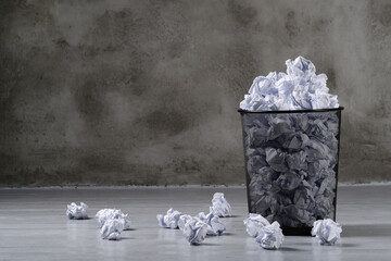 Many creased white paper balls in a trash can on a dark background