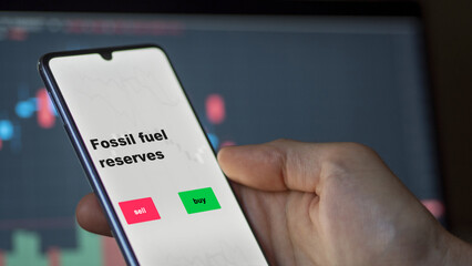 An investor's analyzing the fossil fuel reserves etf fund on screen. A phone shows the ETF's prices stocks to invest