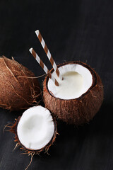 Fresh tasty juicy coconut drink with straw on dark background