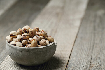 Image of pistachio nuts in bowl isolated on a wooden background.