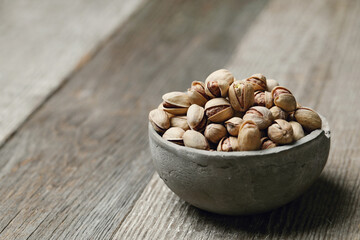 Image of pistachio nuts in bowl isolated on a wooden background.