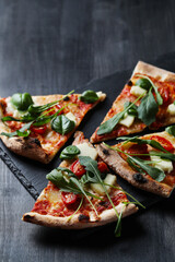 Slices of delicious pizza with cheese, tomato and spinach on a black background