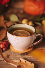 A cup of hot tea with lemon on an autumn background. Autumn and fall vertical postcard. Thanksgiving day or halloween concept.