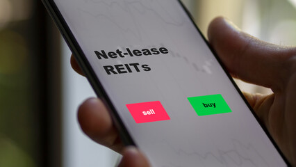 An investor's analyzing the reit on screen. A phone shows the ETF's prices net-lease REITs