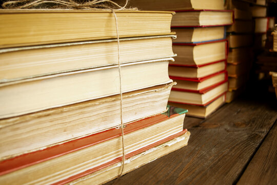 Books tied with string stand on a wooden table. Several books are put together. A stack of books on the wooden table.