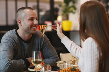 A young woman feeds her lover spaghetti at a romantic dinner at a restaurant