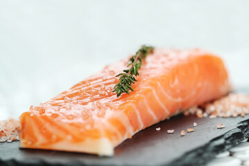 Fresh juicy raw salmon with rosemary and sea salt on a black cutting board