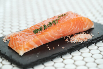Fresh juicy raw salmon with rosemary and sea salt on a black cutting board