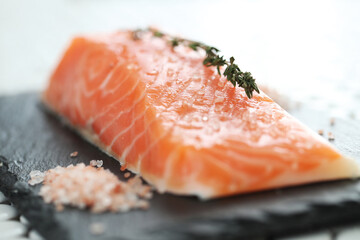 Close view of fresh juicy raw salmon with rosemary and sea salt on a black cutting board