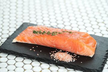 Fresh juicy raw salmon with rosemary and sea salt on a black cutting board

