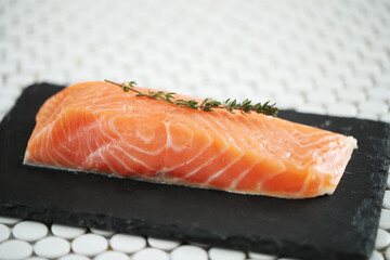 Close view of fresh juicy raw salmon with rosemary on a black cutting board