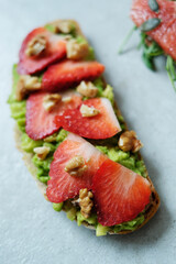 Close view of delicious sweet Bruschetta (sandwiches) with smashed avocado and slices of strawberry on a white background