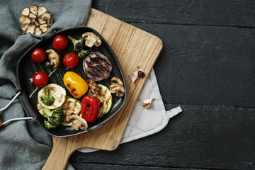Image of tasty hot grilled food with various vegeables in a black pan on a wooden cutting board