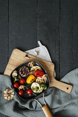 Top view of tasty hot grilled food with various vegeables in a black pan on a wooden cutting board