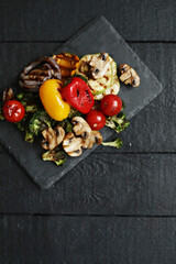 Picture of tasty hot grilled food with various vegeables on a black wooden cutting board