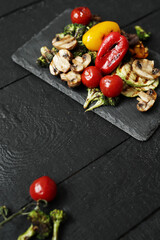 Picture of tasty hot grilled food with various vegeables on a black wooden cutting board
