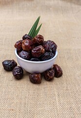 Closeup of Organic Date Palm Fruit or Phoenix Dactylifera in a White Bowl Isolated on Burlap Fabric Background in Vertical Orientation