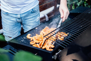 Grilling shrimp on skewer on outdoor grill. Grilled shrimps on the flaming grill. Man hand using...