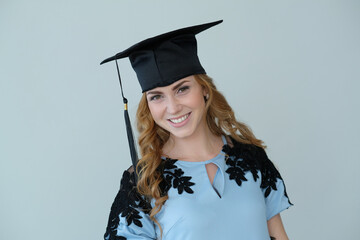 Photo of young smiling woman in beautiful dress in graduation hat posing for camera