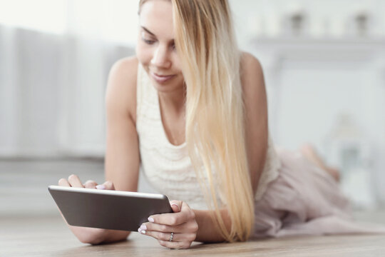 A photo of a young beautiful woman using a digital tablet and lying on the floor