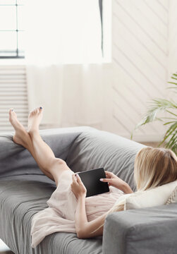 A picture of a beautiful young woman using a digital tablet and lying on the couch