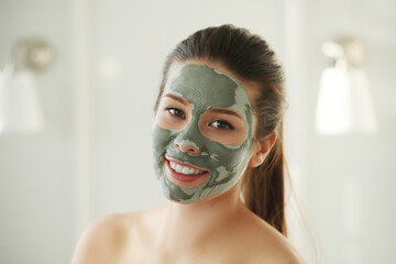 Close up portrait of smiling attractive young woman with green clay mask at the spa salon