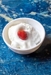 Melting Ice Cream with Ripe Strawberry Slice in White Bowl Isolated on Bluish Background in Vertical Orientation